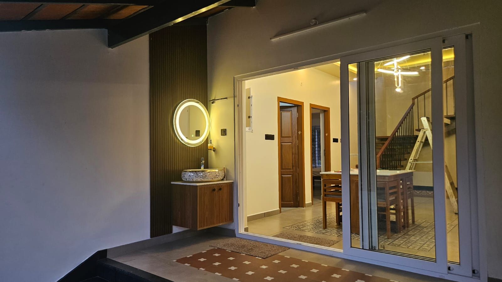 Semi-outdoor wash area featuring a circular illuminated mirror, wooden vanity, and large sliding glass doors leading into the main living space.