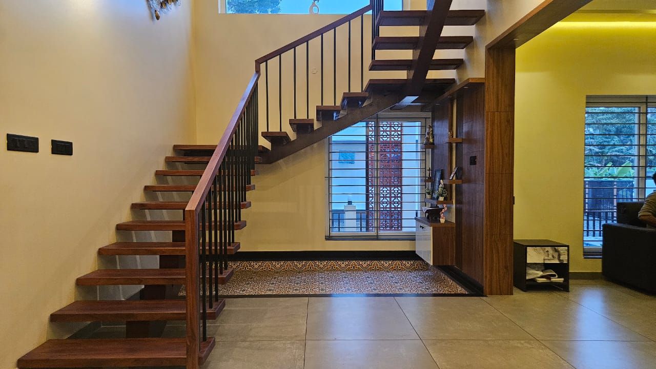 Interior view of a modern wooden staircase with black metal railings, positioned over a patterned tile floor inlay and adjacent to a custom wooden shelving unit.