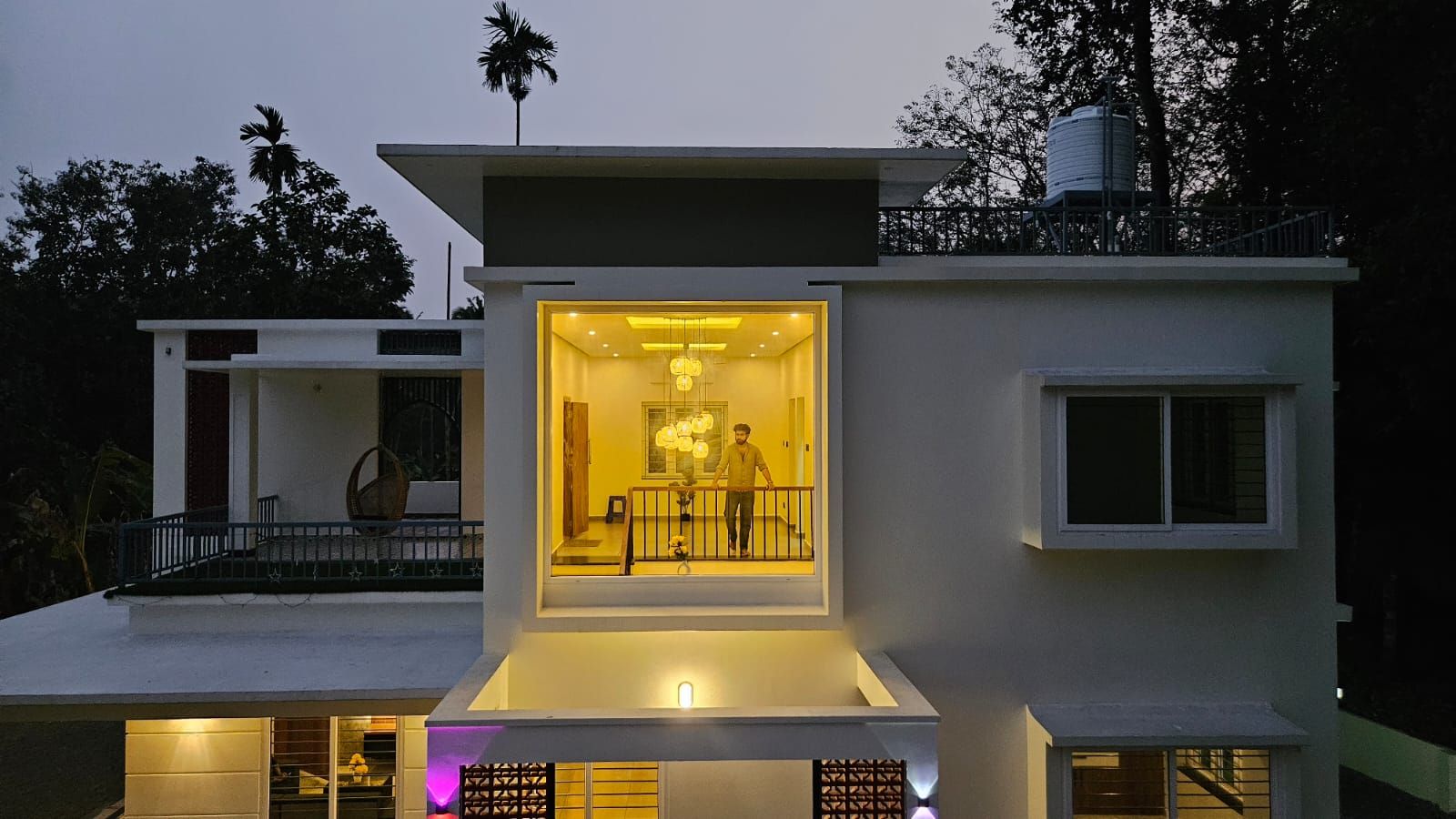 Nighttime exterior facade featuring a prominent framed window box glowing with warm interior light, revealing a resident on the upper landing.