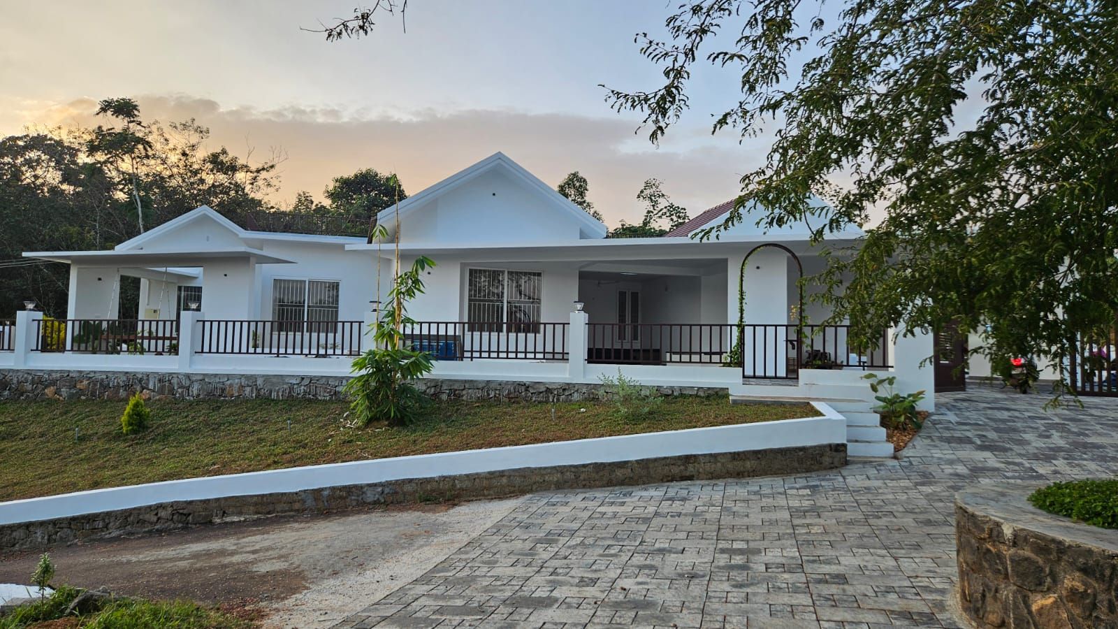 Front elevation of the sprawling white residence with gabled roofs, a dark-railed verandah, and a paved walkway.