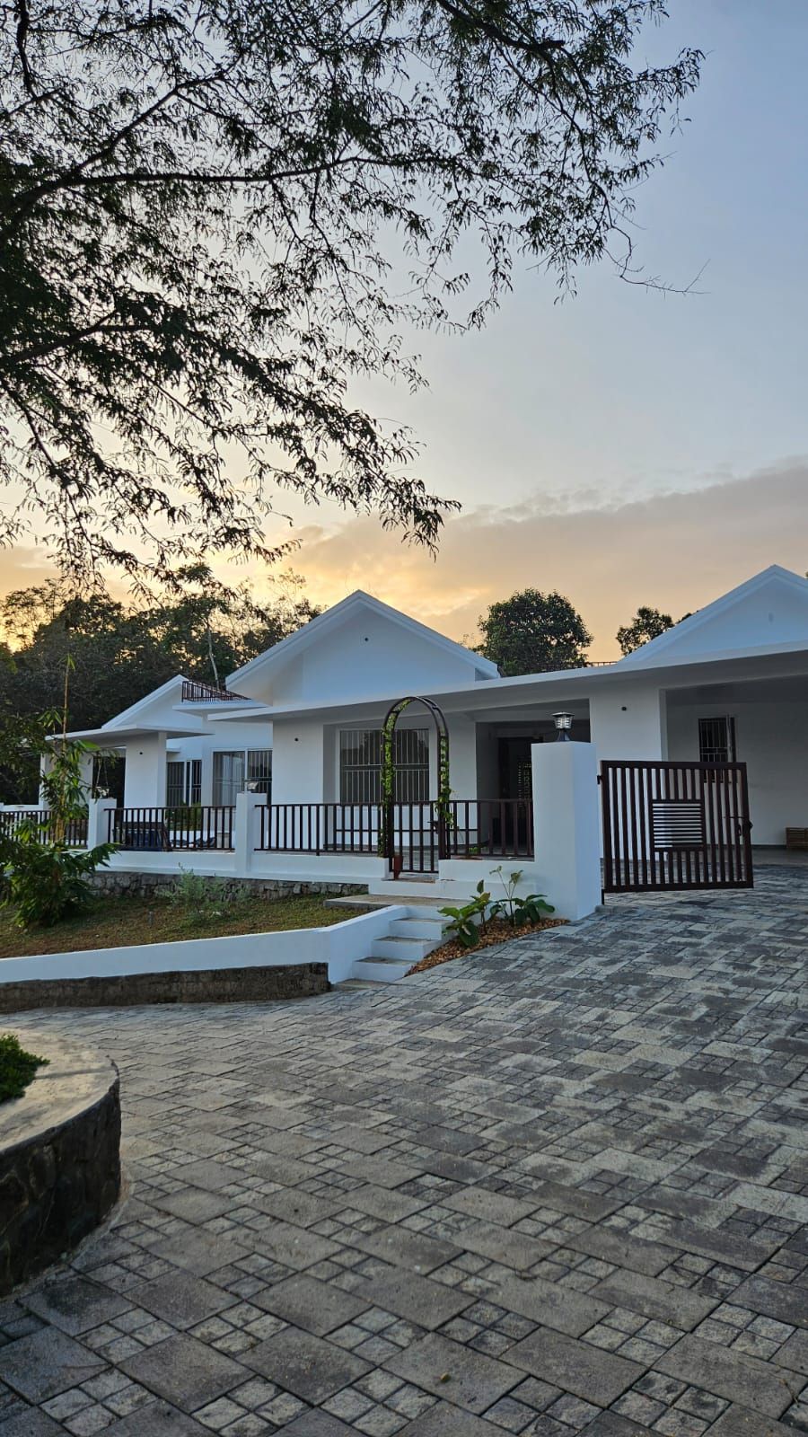 View of the home's paved stone driveway and entrance gate at sunset, with the modern white facade in the background.