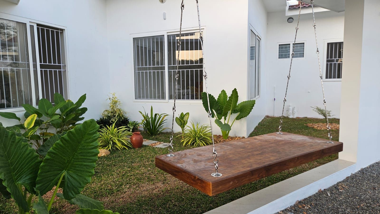 Lush internal courtyard featuring a large wooden swing and tropical landscaping against white walls.
