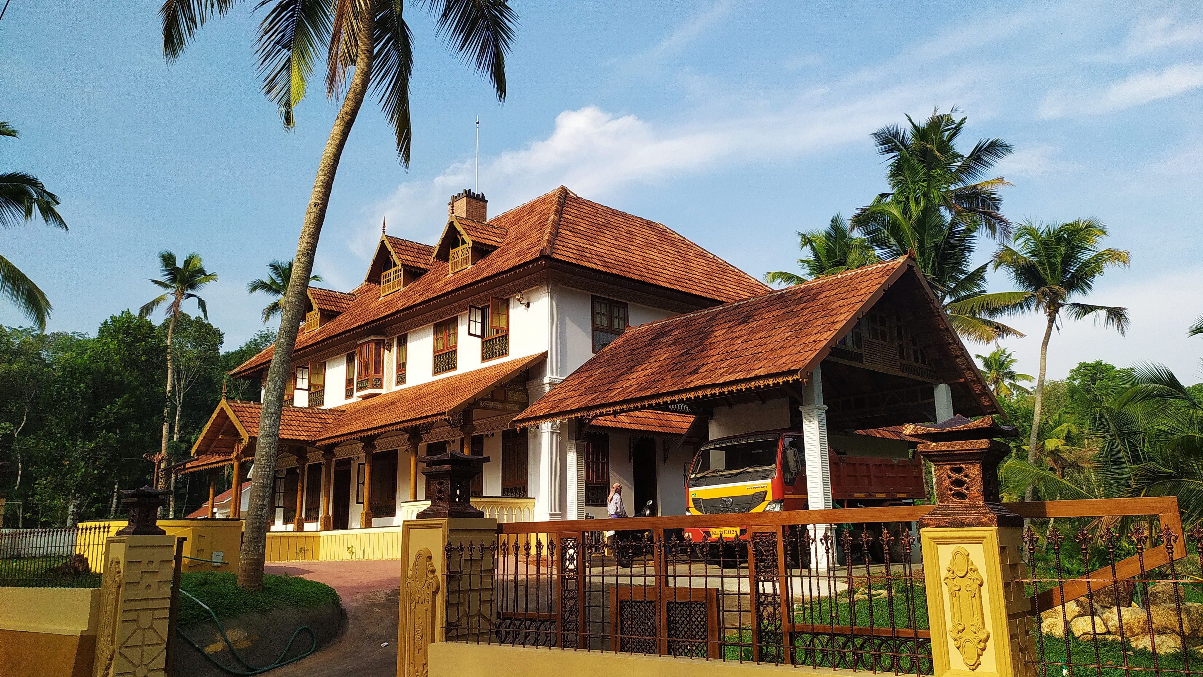 Angled view of the Kerala-style mansion, showing the intricate wooden pillars and multi-level roof design.